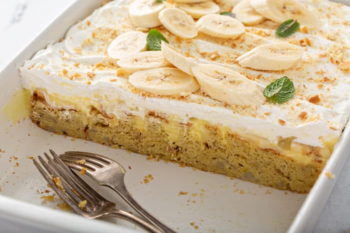 Banana pudding poke cake in a white baking dish with several slices removed to show the inside view of the cake