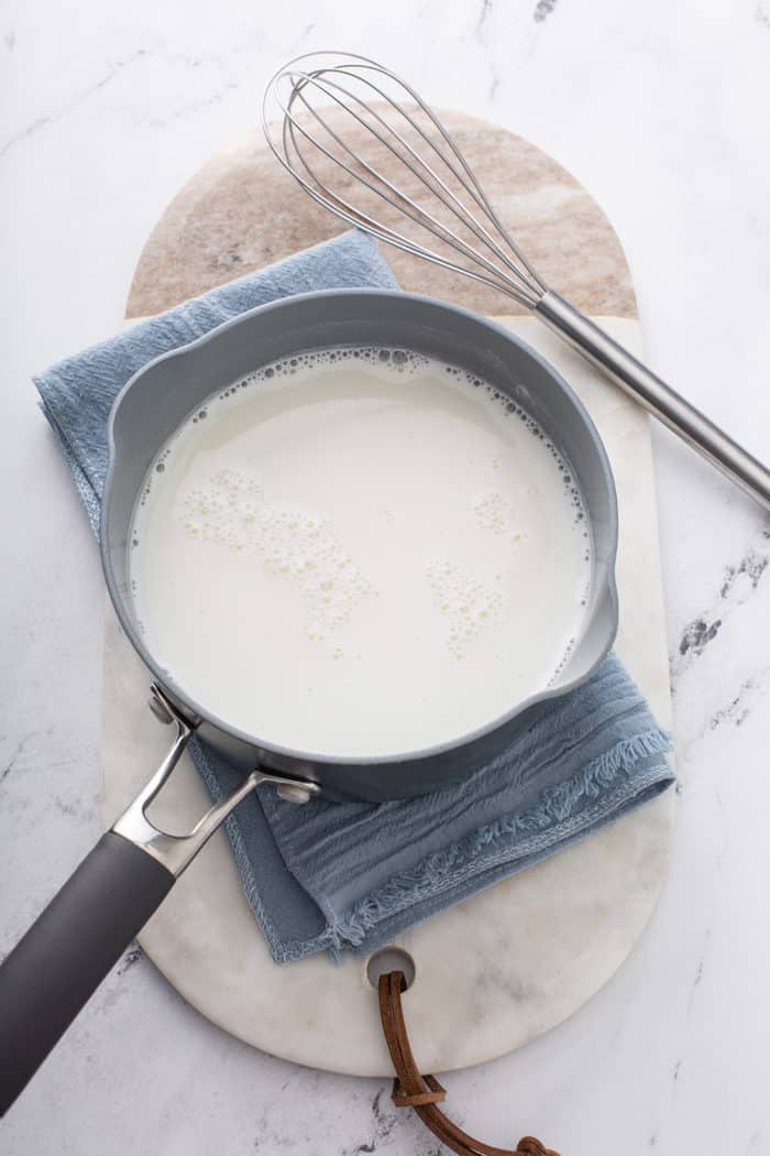 Milk and sugar in a saucepan set on a blue towel on a marble countertop