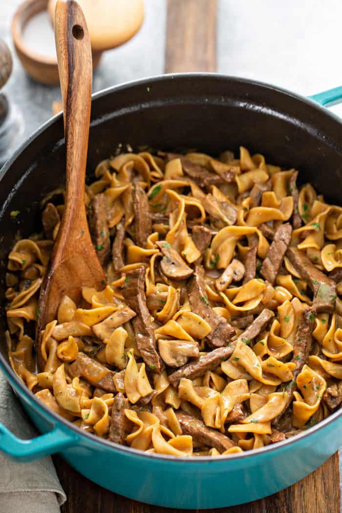 Wooden spoon stirring one-pot beef stroganoff in a large dutch oven