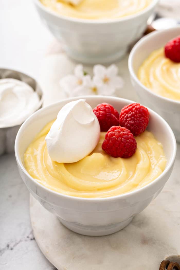Vanilla pudding in a small white bowl, topped with whipped cream and fresh raspberries
