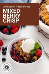 Serving of berry crisp topped with ice cream in a white bowl. A bowl of berries and the rest of the crisp is in the background. Text overlay includes recipe name.
