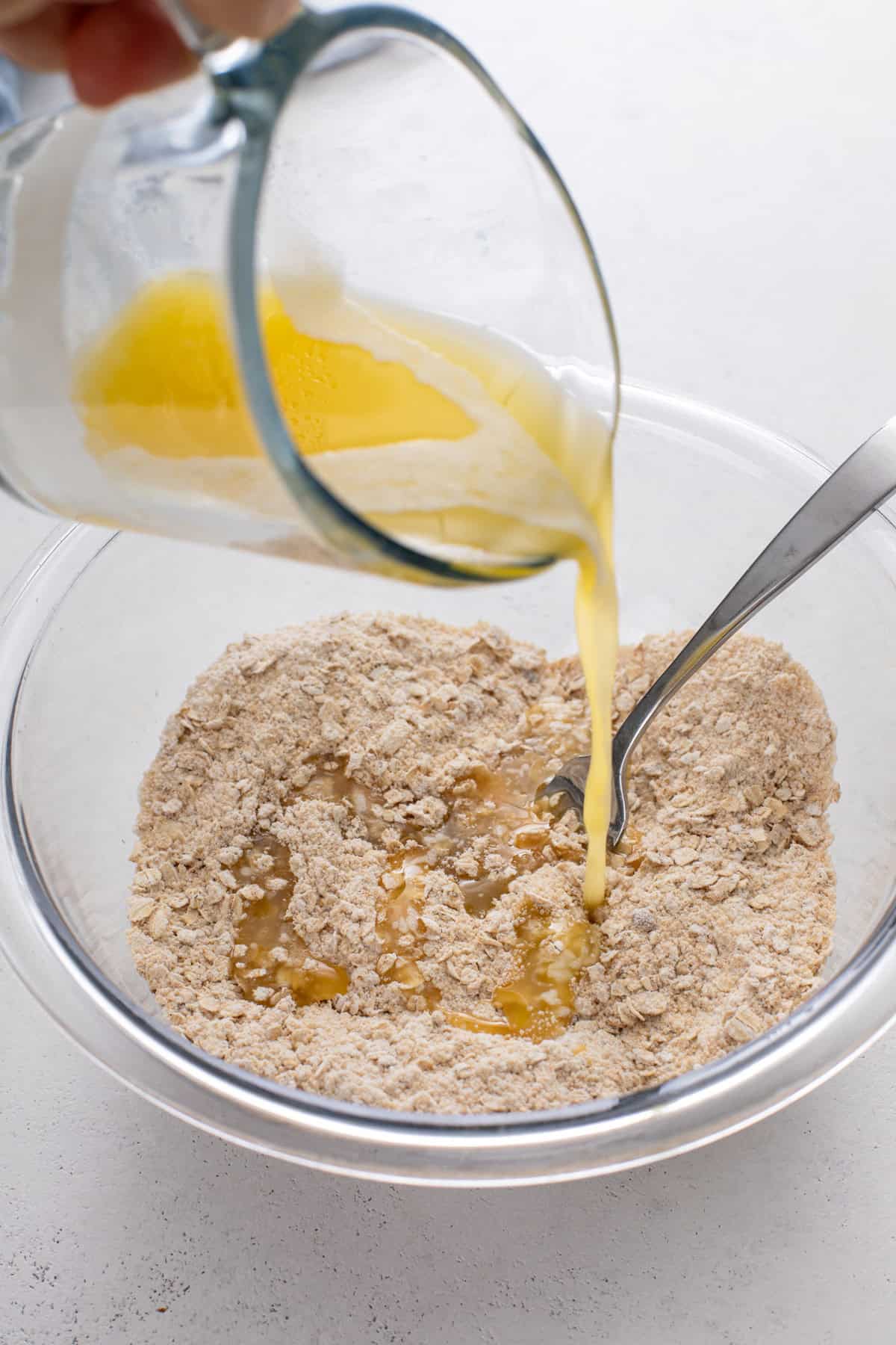 Melted butter being drizzled into the dry ingredients for crisp topping.