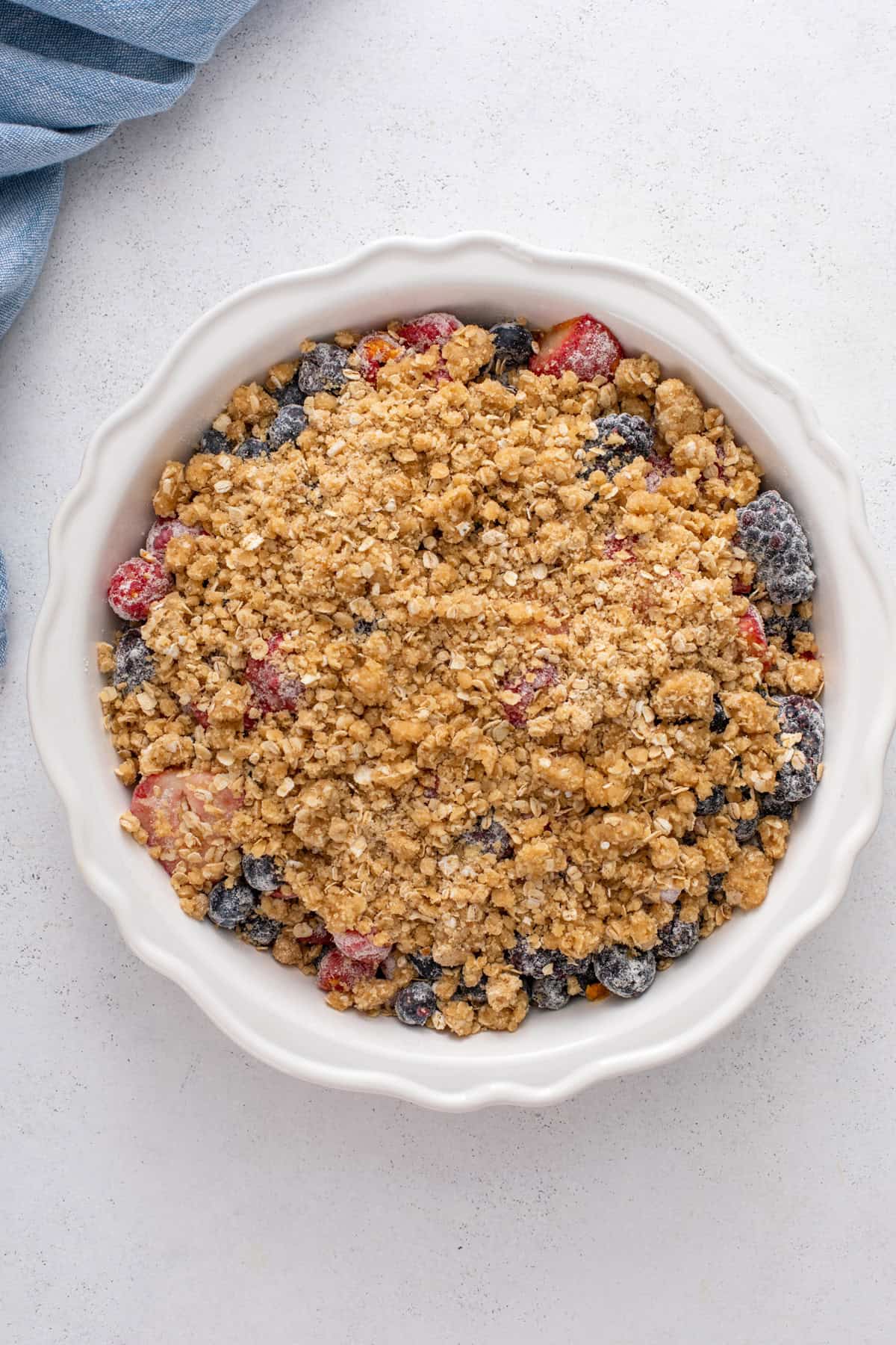 Berry crisp assembled in a white baking dish, ready to go in the oven.