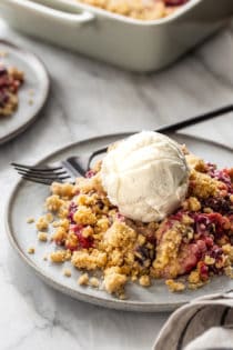 Close up of berry crisp topped with vanilla ice cream on a gray plate