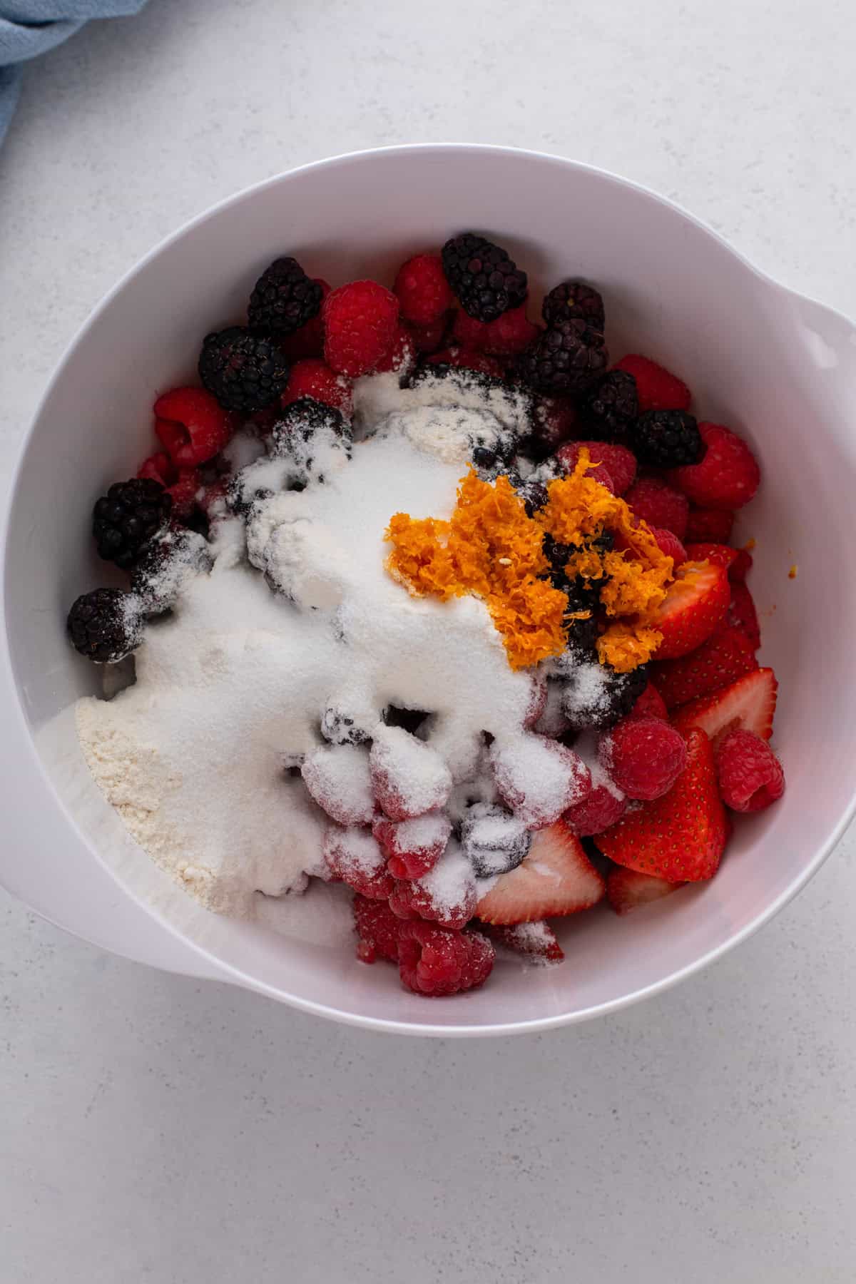 Ingredients for mixed berry crisp filling added to a white bowl.