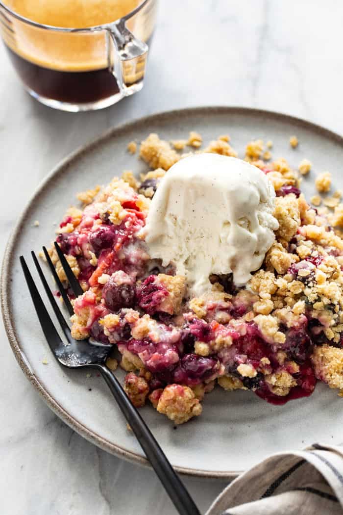 Fork next to berry crisp on a gray plate, with vanilla ice cream starting to melt on top of the crisp