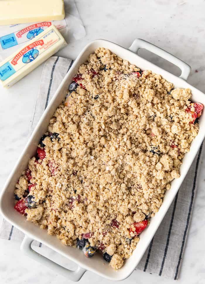 Overhead view of mixed berry crisp assembled in a white baking dish, ready to bake
