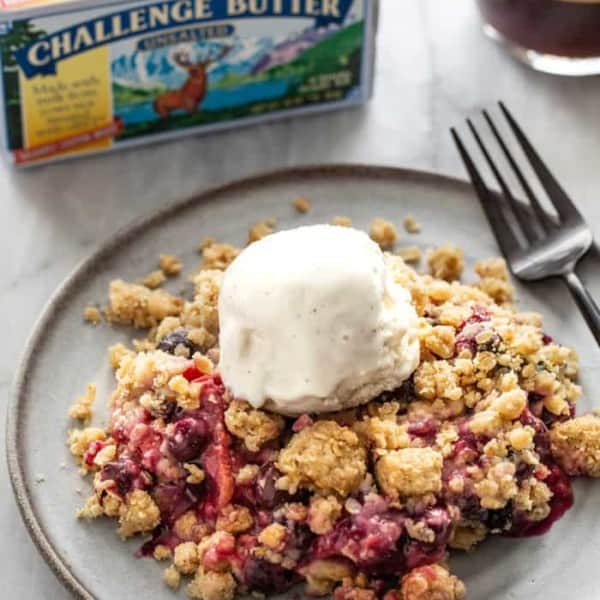 Plate of berry crisp topped with a scoop of vanilla ice cream, with a carton of butter in the background