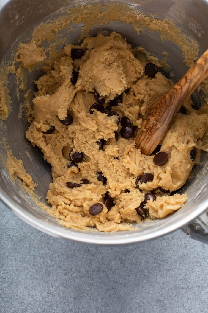Wooden spoon stirring together brown butter chocolate chip cookie dough in a metal mixing bowl