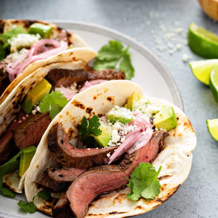 Close up of a flank steak taco in a flour tortilla, topped with avocado, pickled onion and cilantro