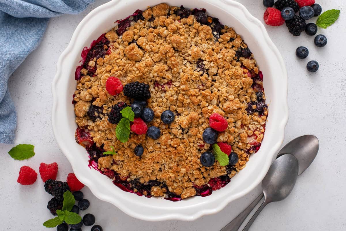Cooled berry crisp in a white baking dish, garnished with mint and fresh berries.