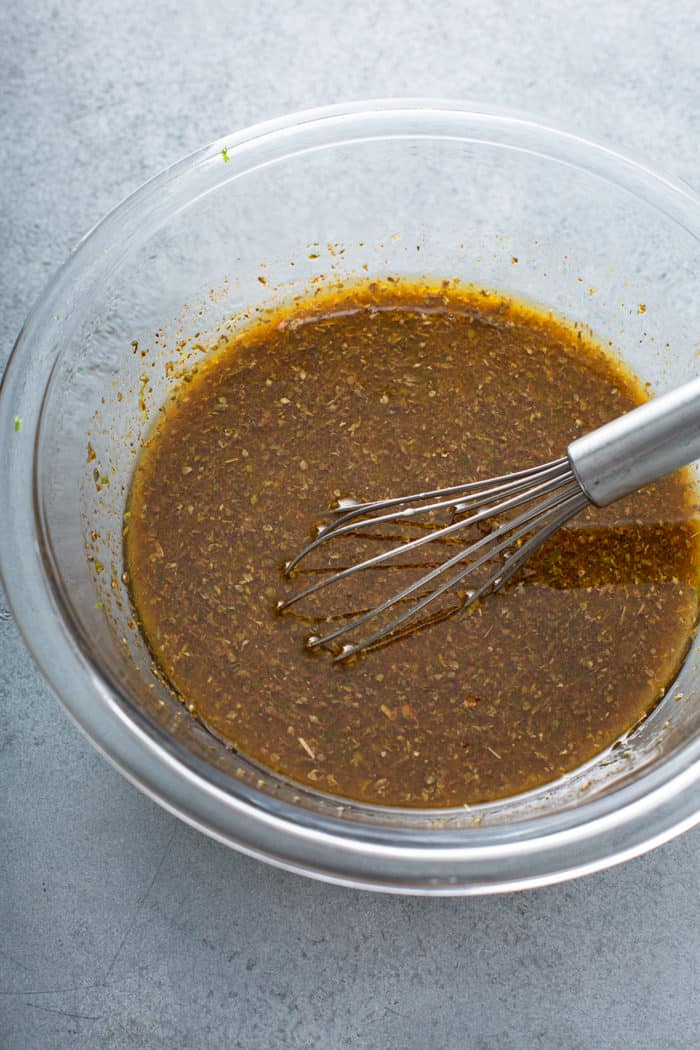 Whisk stirring together flank steak marinade in a glass bowl on a gray counter