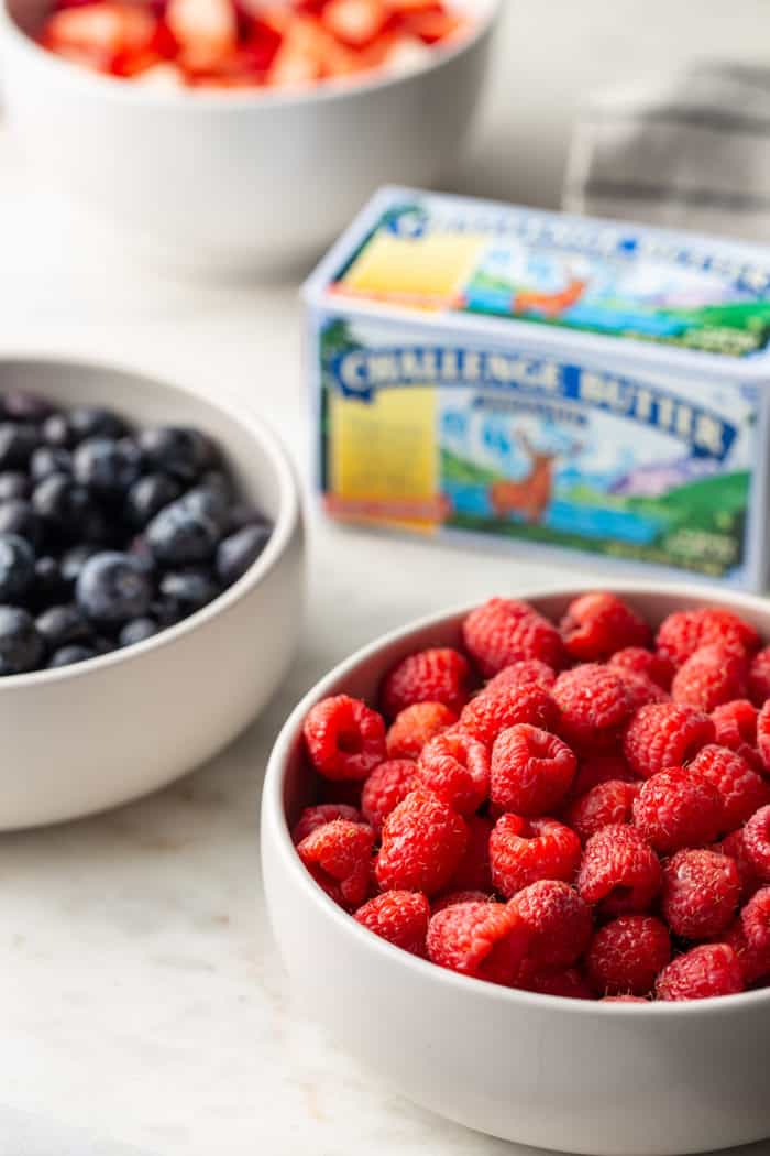 White bowls of fresh berries surrounding a carton of butter on a marble countertop