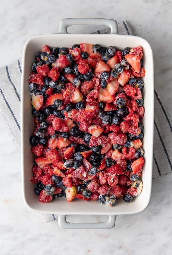 Filling for mixed berry crisp in a white baking dish on a marble countertop