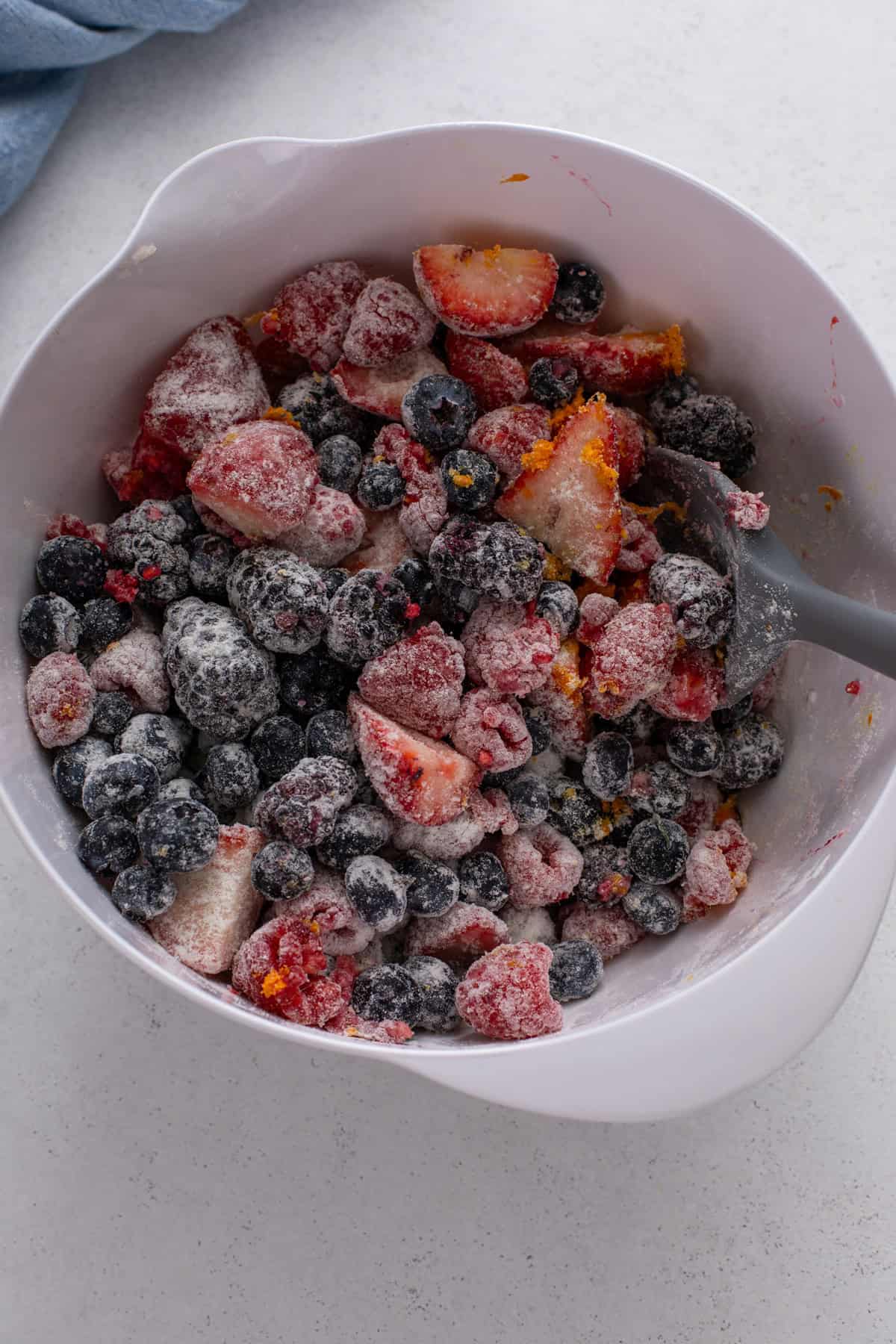 Spatula mixing berry crisp filling in a white bowl.