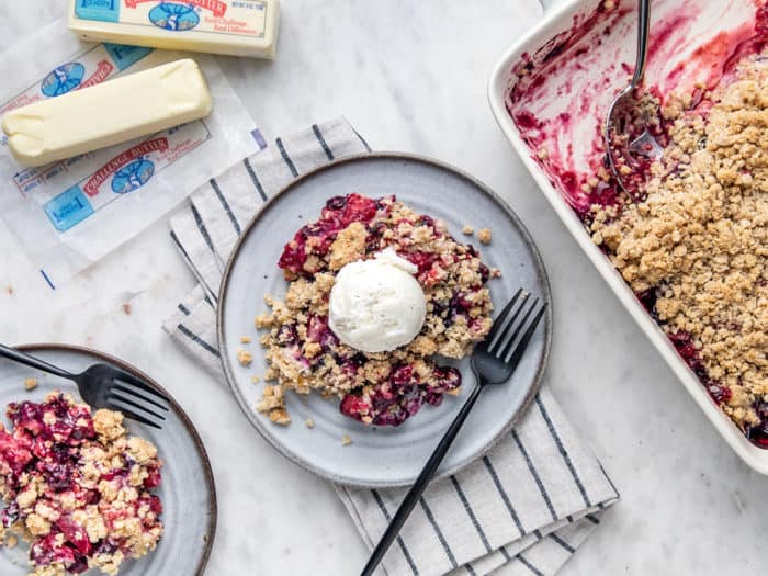 Overhead view of two plates of berry crisp, topped with ice cream, next to a baking dish of crisp and sticks of butter