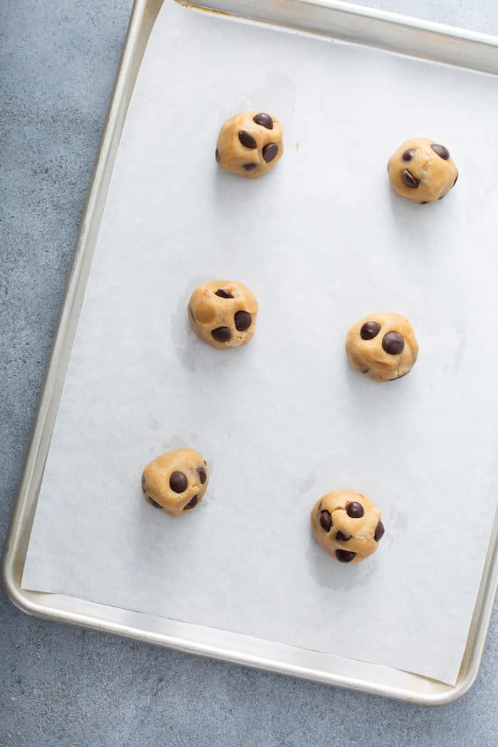 Six balls of brown butter cookie dough set on a parchment-lined baking sheet