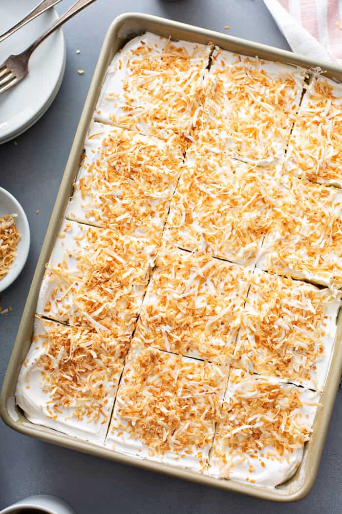 Sliced coconut poke cake in a cake pan, set on a gray countertop