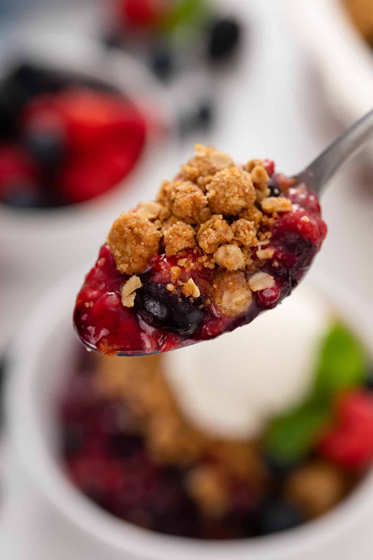 Spoon holding up a bite of mixed berry crisp.