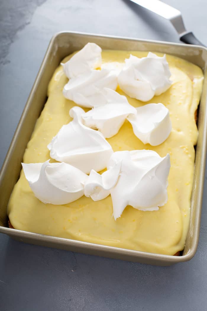 Dollops of cool whip on top of a pudding-topped poke cake in a cake pan
