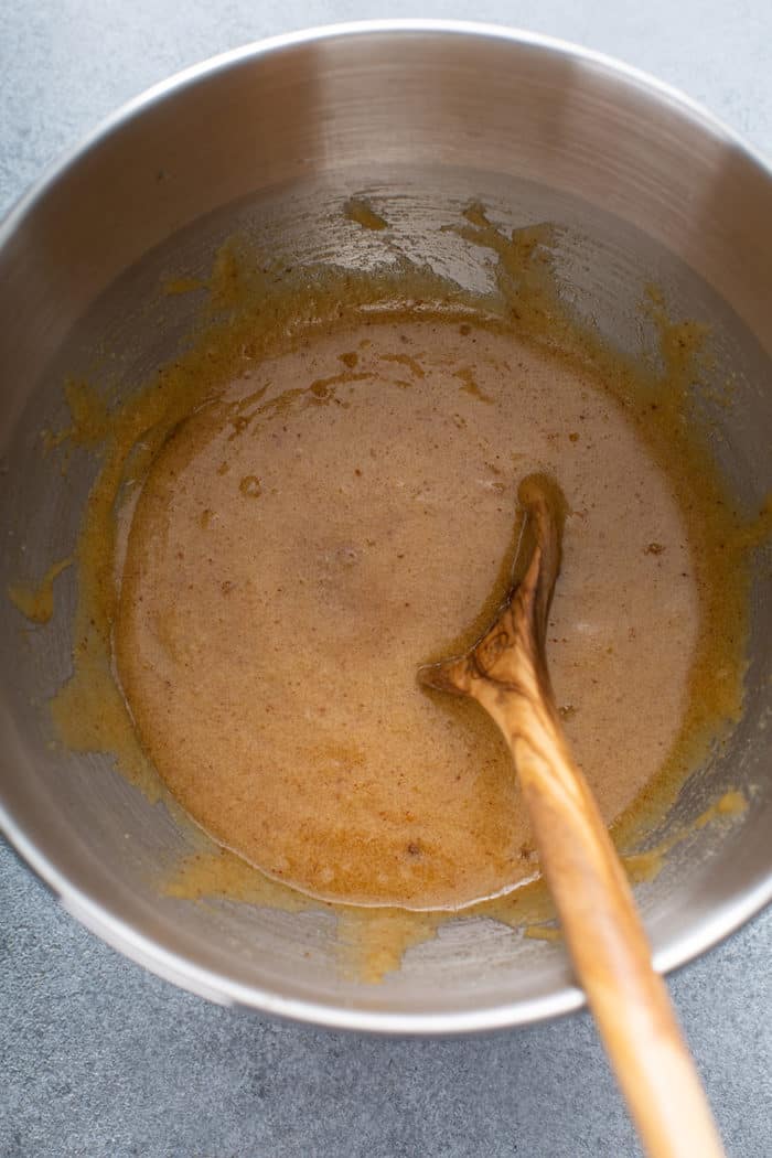 Spoon stirring together the wet ingredients for brown butter chocolate chip cookies in a metal mixing bowl