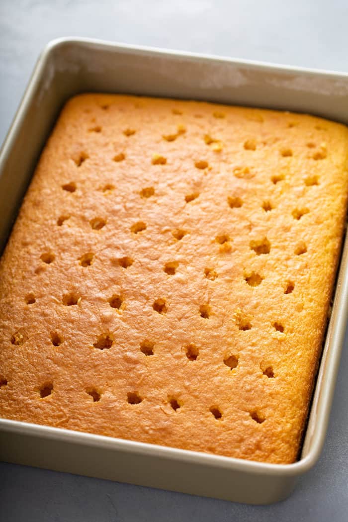 Baked yellow cake in a cake pan, with holes poked in it to turn it into a poke cake