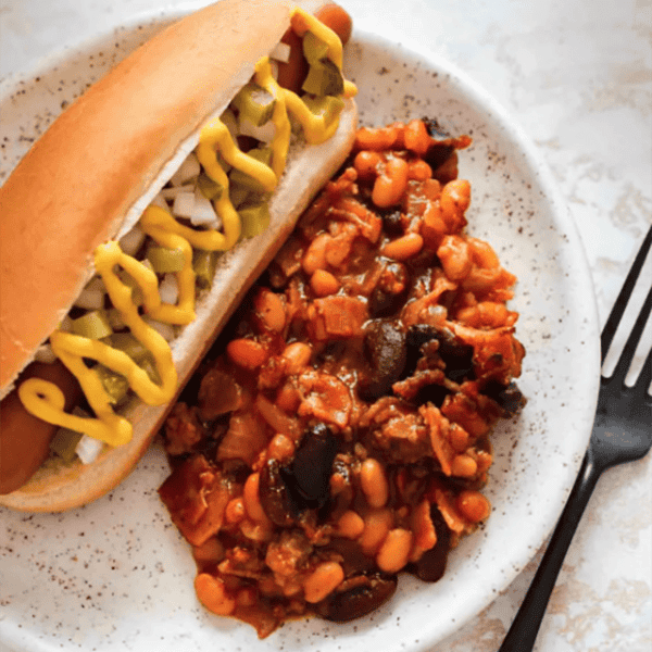 Old fashioned baked beans on a plate next to a hot dog