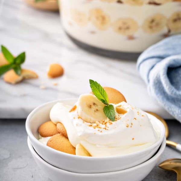 Magnolia bakery banana pudding in a small white serving dishes, with a trifle dish of the pudding in the background