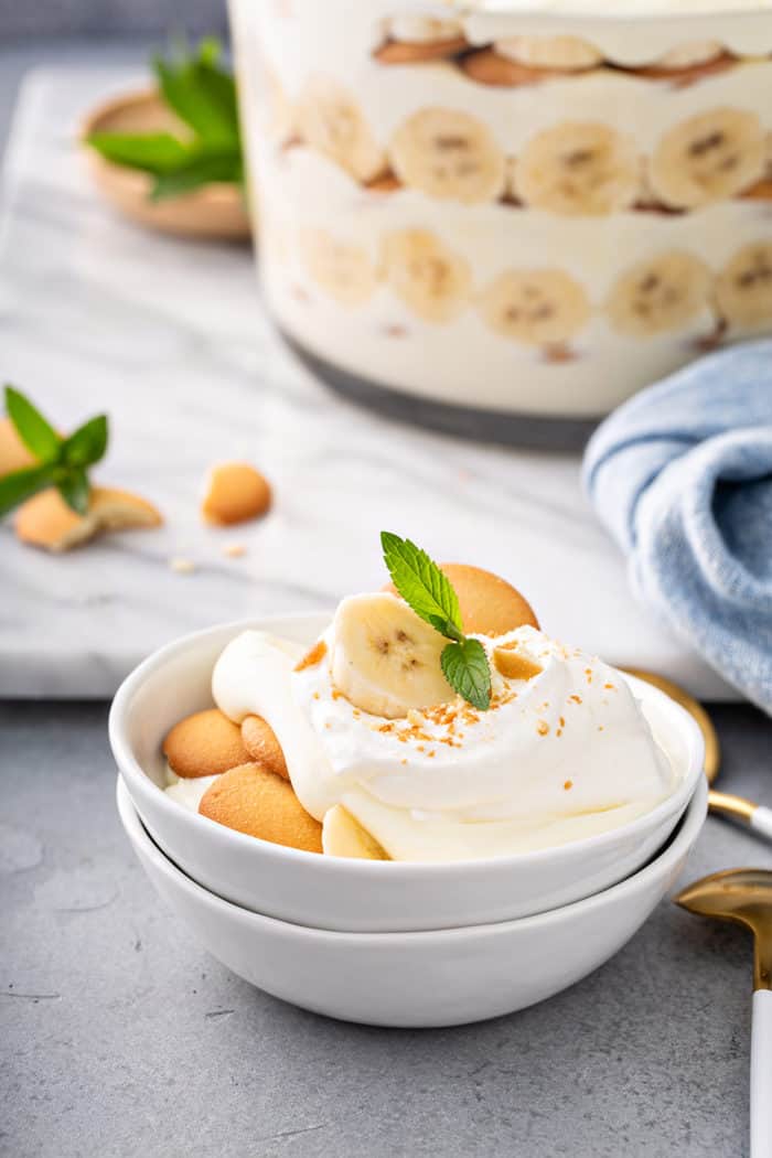 Magnolia bakery banana pudding in a small white serving dishes, with a trifle dish of the pudding in the background