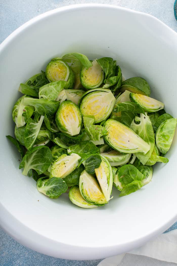 Prepped brussels sprouts tossed with olive oil and salt in a white mixing bowl