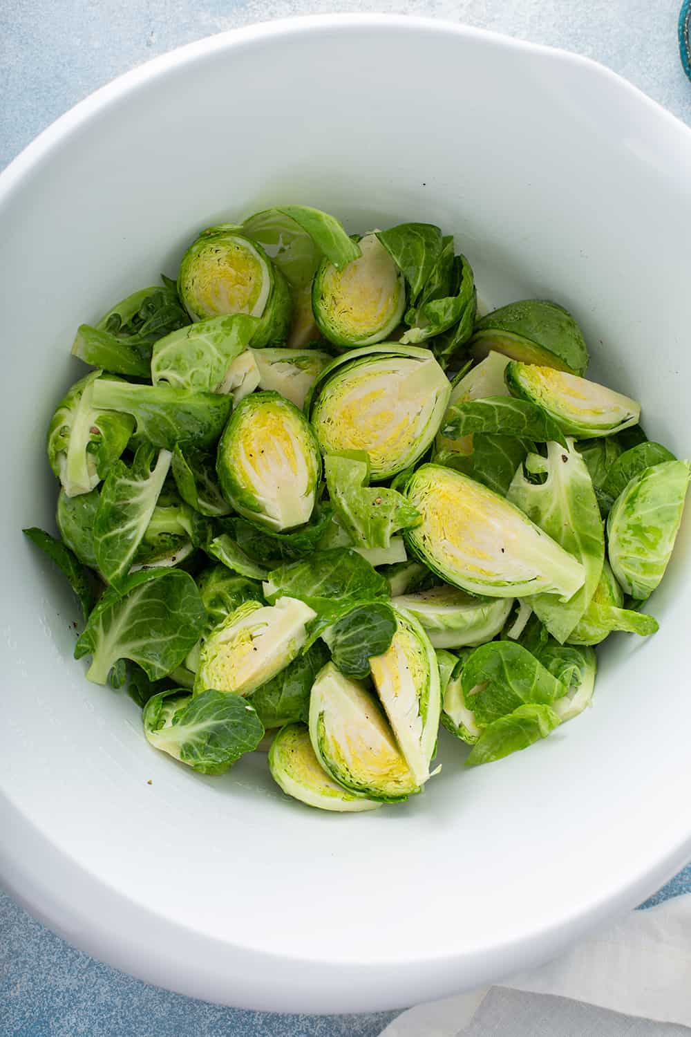 Prepped brussels sprouts tossed with olive oil and salt in a white mixing bowl