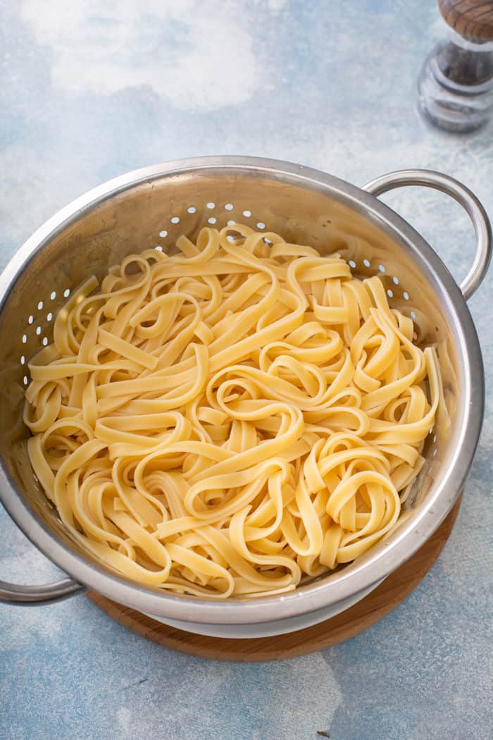 Cooked fettuccine pasta in a metal colander on a blue counter