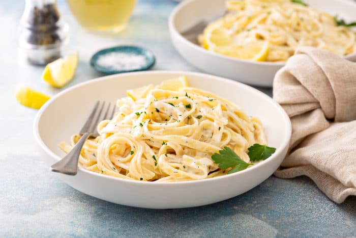 Easy fettuccine alfredo in a white pasta bowl with a fork, with a second bowl of pasta in the background