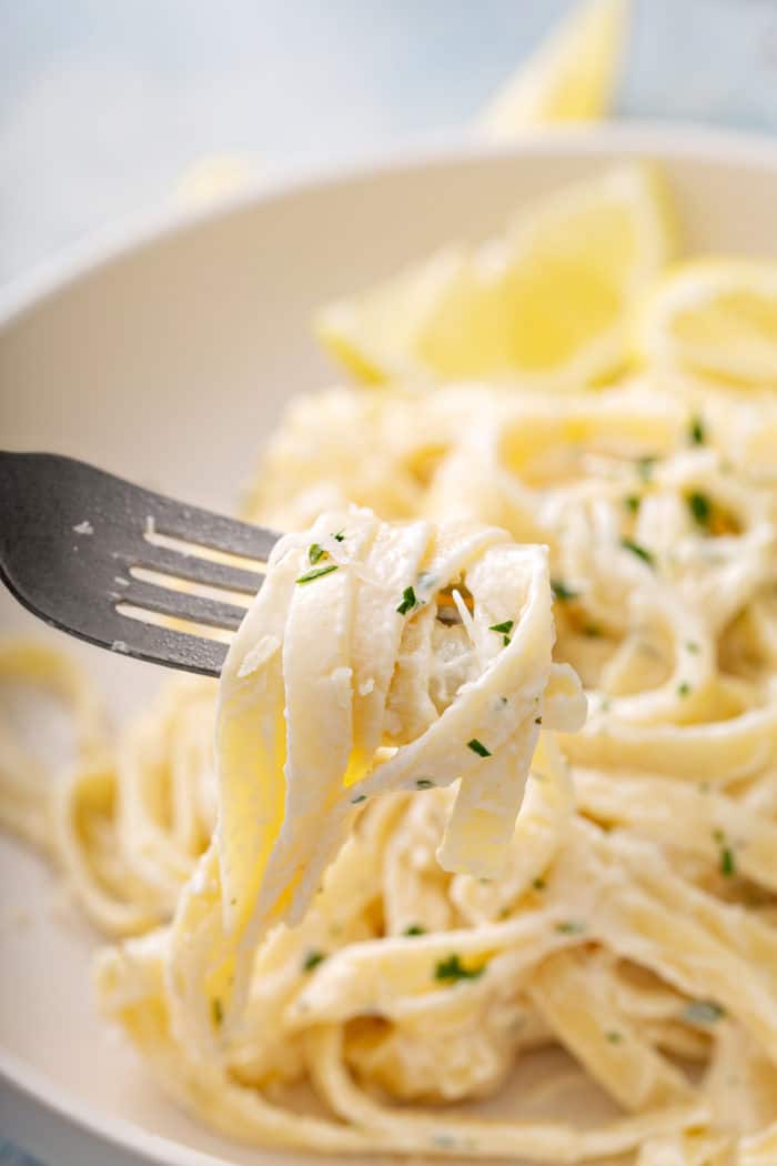 Fork picking up a bite of fettuccine alfredo from a white pasta bowl