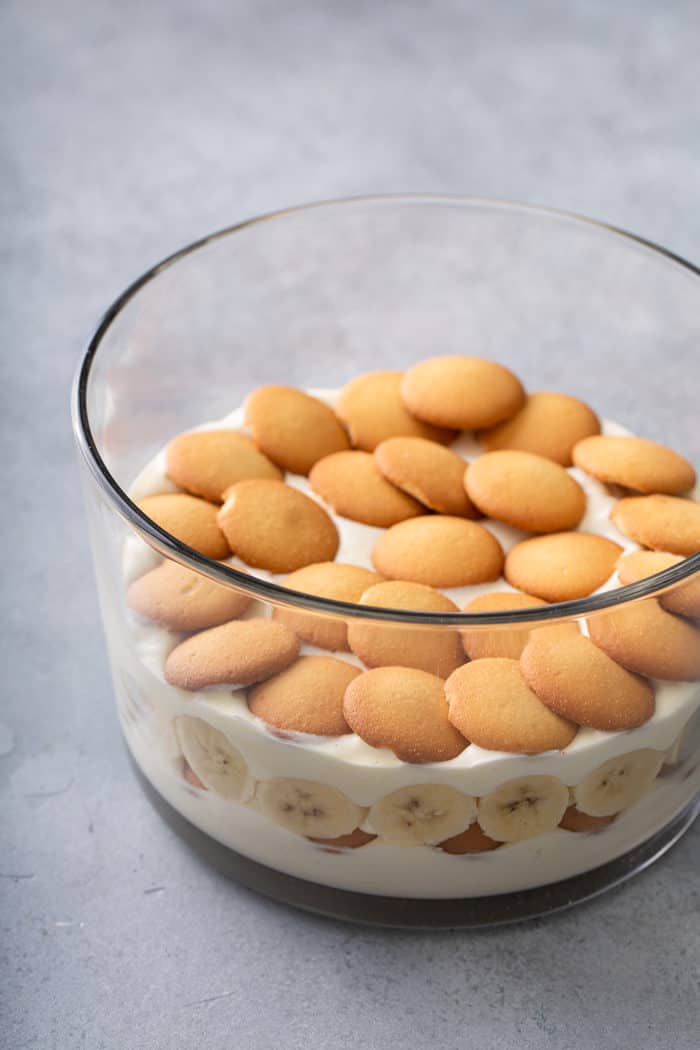 Layers of pudding, bananas, and vanilla wafers being assembled in a trifle dish