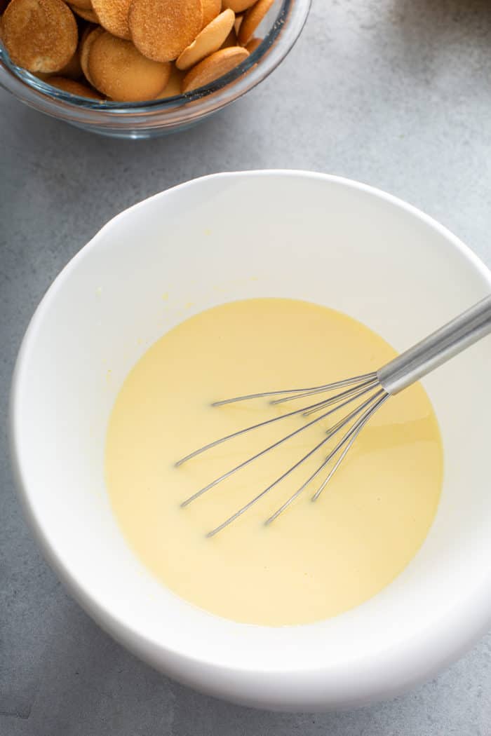 Whisk combining vanilla pudding and condensed milk in a white mixing bowl