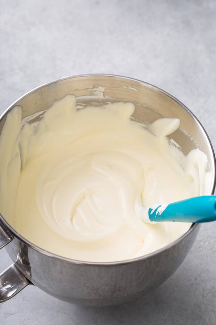 Spatula folding together vanilla pudding and whipped cream in a metal mixing bowl