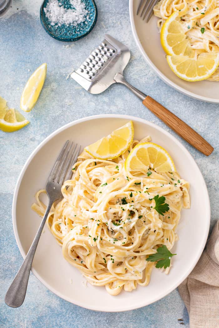 Overhead view of a plate of easy fettuccine alfredo garnished with fresh parsley and lemon wedges