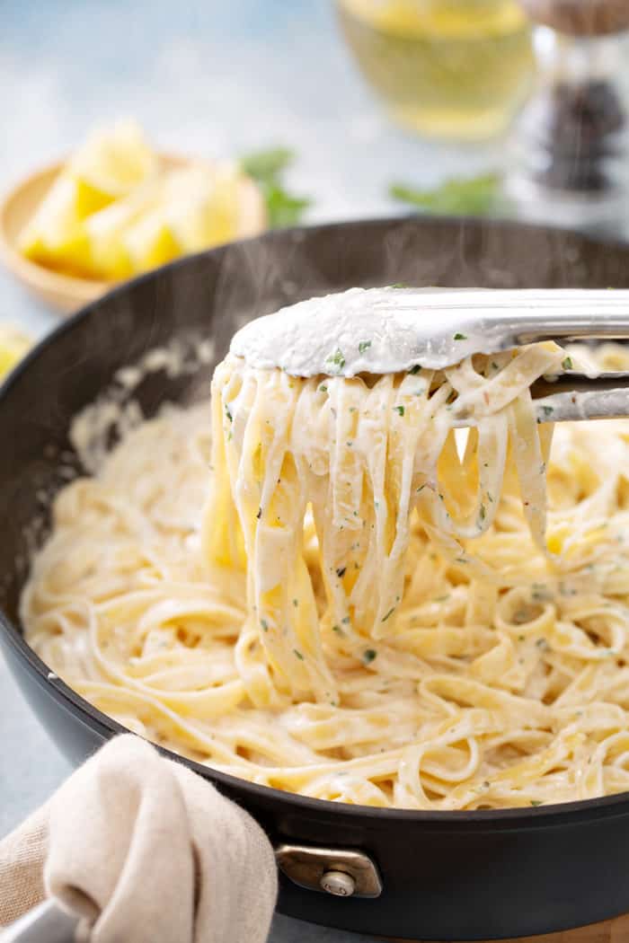 Tongs picking up a serving of fettuccine alfredo out of a skillet