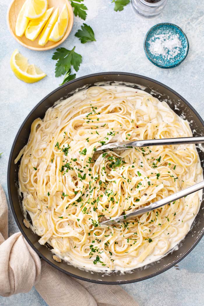 Tongs tossing together fettuccine alfredo in a black skillet