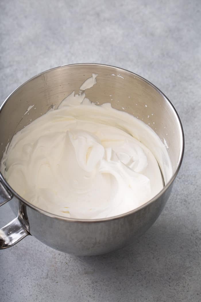 Whipped cream in a metal mixing bowl on a gray countertop