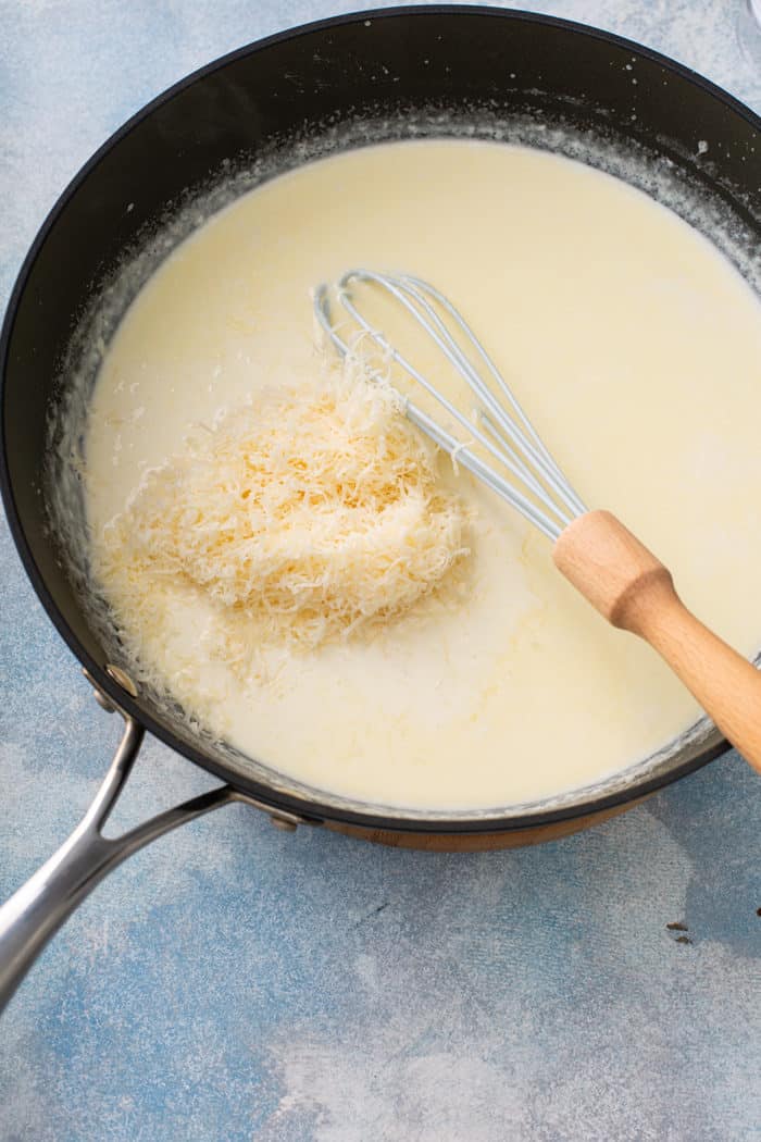 Whisk stirring grated parmesan cheese into alfredo sauce in a skillet