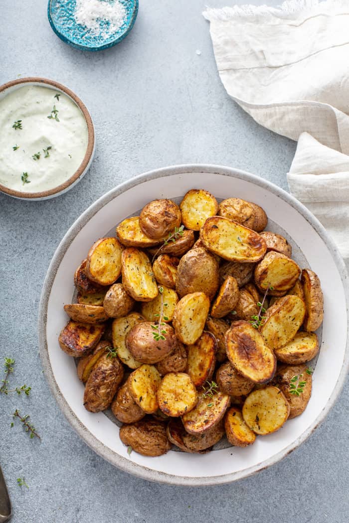 Bowl of air fryer roasted potatoes on a gray countertop next to a napkin and a ramekin of aioli