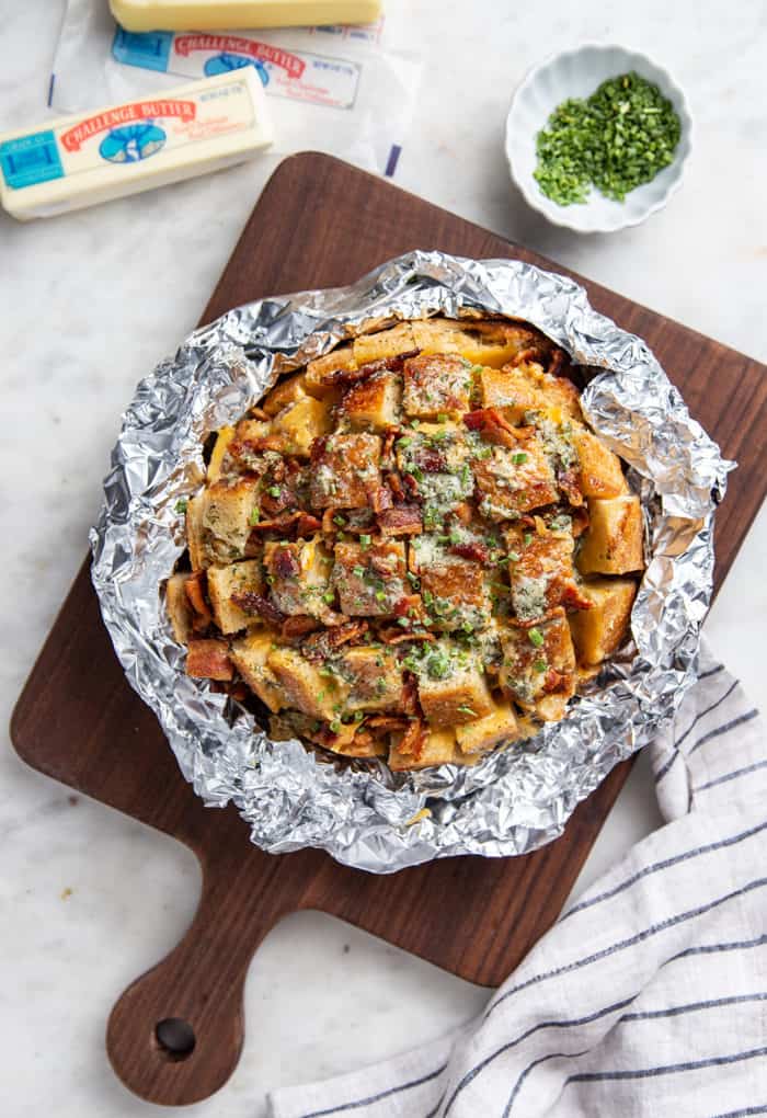 Overhead view of a baked loaf of cheesy ranch pull apart bread, wrapped in foil and set on a cutting board