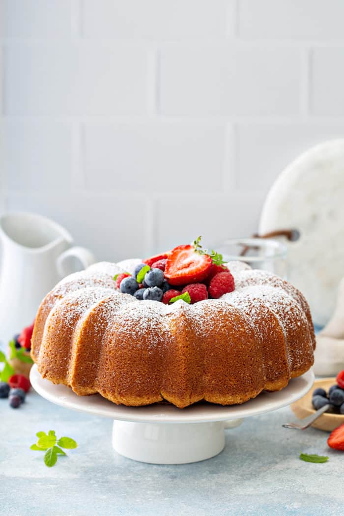 Baked whipping cream cake on a white cake stand, garnished with powdered sugar and fresh berries