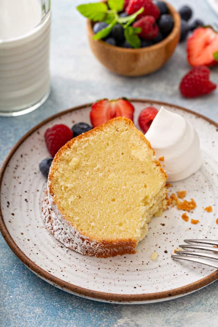 Slice of whipping cream cake with a bite taken out of it on a plate next to berries and whipped cream