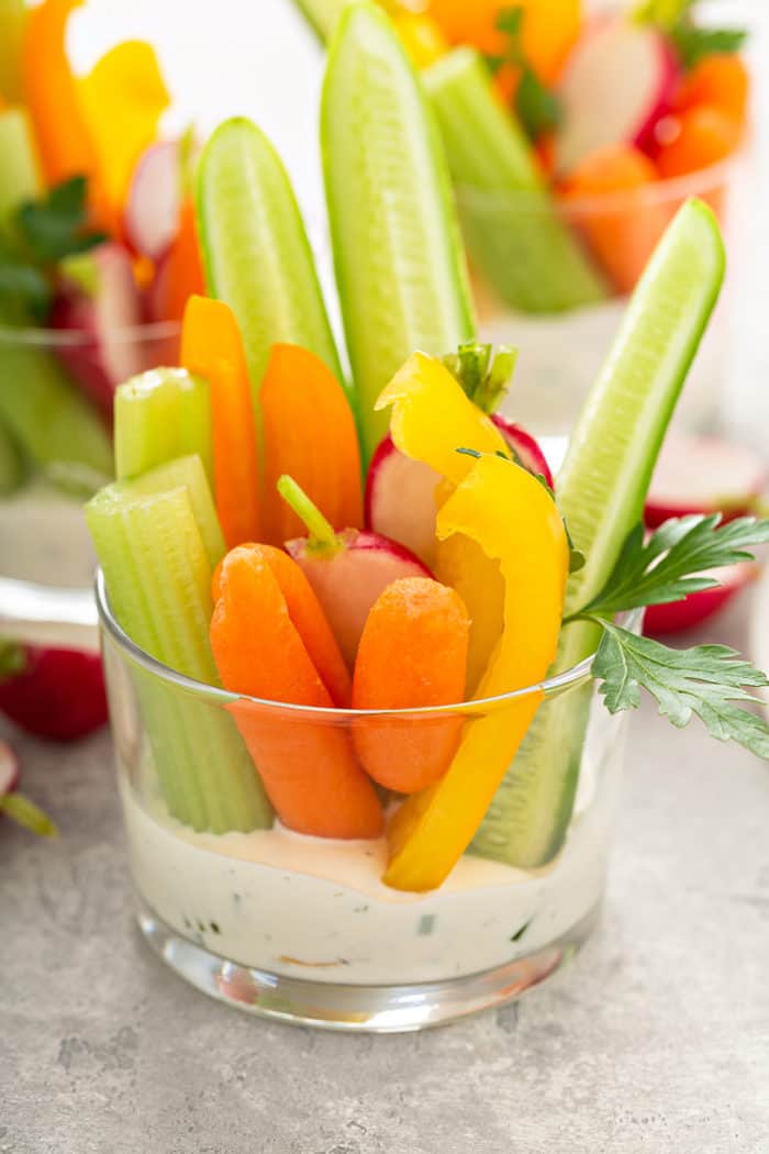 Taza de vidrio con salsa ranch en la parte inferior y verduras cortadas en la salsa