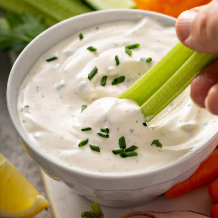 Celery stick being dipped into a bowl of homemade ranch dip