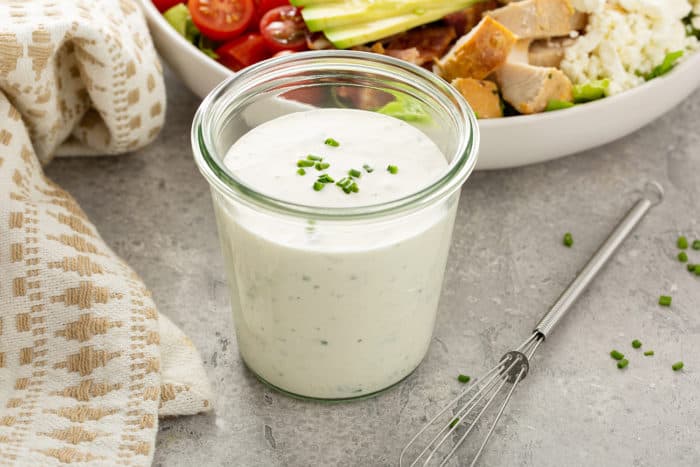 Jar of homemade ranch dressing next to a bowl of salad
