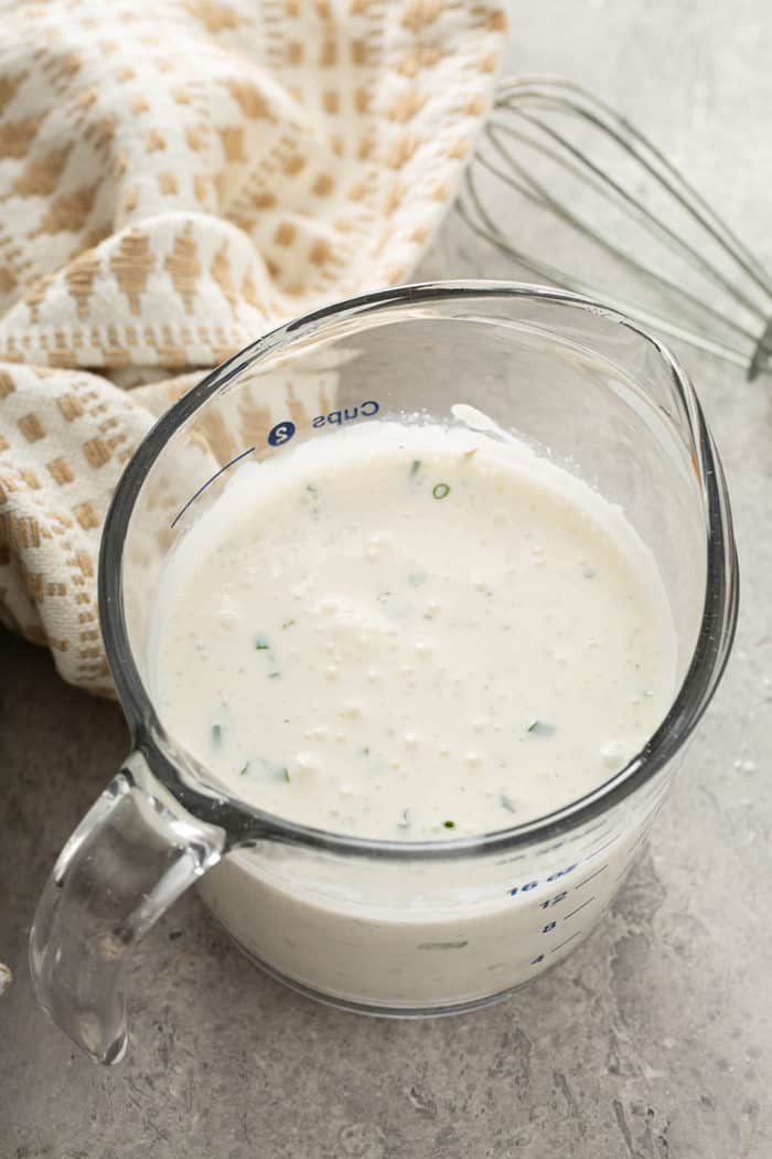 Homemade ranch dressing in a glass measuring cup on a gray countertop